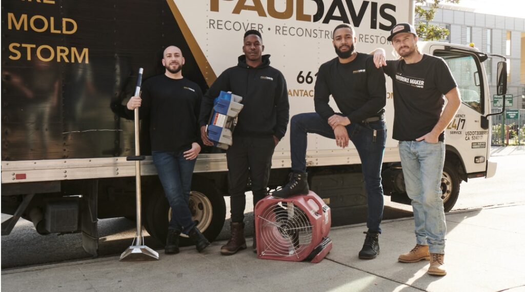 Paul Davis Restoration team members standing beside a branded service truck with restoration equipment, including a commercial air mover and cleaning tools, ready for emergency property restoration services | Paul Davis Restoration of Tri-County, MD